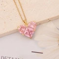 Pink heart crystal pendant on golden chain necklace over a textured stone background - Big Heart Happy