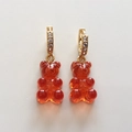 Close-up of orange resin gummy bear earrings with gold hoops and inlaid cubic zirconia - Transparent Red