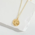 Elegant gold necklace with embossed round fish and wave pendant on white stone base - Fish Wave Gold