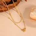 Detail of gold double-layer snake chain and bead necklace with bow pendant on wood background - Gold Double Layer Bowknot Necklace