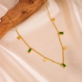 Dettaglio collana dorata con gemme verdi e ciondoli a fiore su legno naturale - Stile Quadrifoglio Strass Quadrato Verde