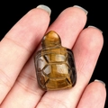 Tiger's eye stone turtle figurine with golden brown stripes held in a hand - Tiger's Eye