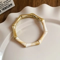 Detalle de brazalete de bambú en metal dorado y resina jaspeada beige sobre plato de cerámica - 4# Brazalete-Dorado-Bambú