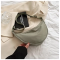 Close-up of a green nylon crescent bag on a bed with a notebook and a glass cup - Army Green
