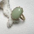 Detailed macro view of handmade gold wire-wrapped ring with green gemstone on coral - Synthetic Light Green Jade