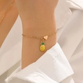 Primo piano di un bracciale dorato con ciondolo a forma di ananas e piccolo cuore - Bracciale Stile Ananas (12385)