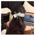 Détail d'une pince à cheveux nœud en ruban à pois blancs sur de longs cheveux bruns ondulés - Pince Torsadée / Blanc