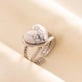 Detail eines herzförmigen Weißtürkis-Rings mit silbernem gedrehtem Band auf Stoff - Silber-Weißer Stein