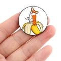 Close-up of circular badge featuring a cartoon Corgi in a banana held by fingers - Corgi in Banana (XZ4708)