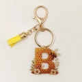 Detalle de llavero abeja letra B dorada con motivo de panal y borla amarilla - Letra B