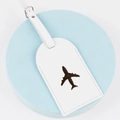 Detail of white leather luggage tag featuring an embossed bronze airplane design - White