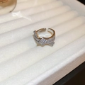 Dettaglio ravvicinato di un anello a torsione argento con zirconi lucenti su vassoio - Stile Aperto Intreccio a Croce / Argento