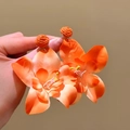 Detailed view of vibrant orange raffia flower earrings held in hand for vacation style. - Orange