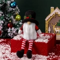 Kerstkabouter knuffelpop met rood zwarte muts en witte baard op een geschenk - Sneeuwpopmuts Stijl