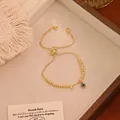 Dettaglio del bracciale a sfere dorate regolabile con occhio greco e lettera F di strass - Lettera L