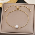 Macro detail of 18k gold chain bracelet with a central white pearl on a silk cushion - Gold Single Pearl Slider Style (5202)