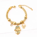 Goldenes Perlenarmband mit Hamsa-Hand und Evil Eye auf weißem strukturiertem Grund - Armband