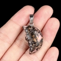Hand holding a crescent moon face carved natural pink rhodonite stone pendant - Rhodonite