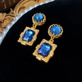 Detailaufnahme von Vintage Gold-Ohrringen mit blauen Kristallen auf schwarzem Samt - Silbernadel-Blau