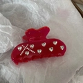 Primer plano de pinza de pelo roja con brillantes corazones sobre papel de seda blanco - Pinza de pelo roja con diamantes de imitación