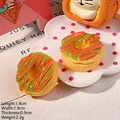Macro detail of miniature resin donut charms with green icing and red stripes on a plate - Matcha Donut