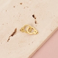 Macro detail of interlocking gold handcuff pendant on a textured stone surface - Gold