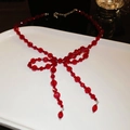 Macro shot of red beaded bow necklace with faceted crystal tassels on a white plate - Crystal Bow Necklace / Red