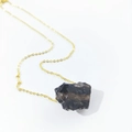 Macro shot of irregular natural dark crystal pendant with a sleek gold chain necklace - Smoky Quartz