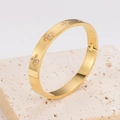 Detail of gold clover bangle with zircon inlays on a travertine stone surface - Gold