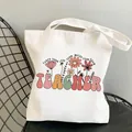 Beige canvas teacher tote bag with floral art and inspirational quote on a chair - Style C6