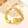 Detail of golden coin link bracelet with lobster clasp and heart charm on beige background - 9-Coin Bracelet