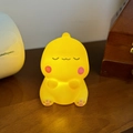 Cute yellow cartoon dinosaur night light with soft warm glow on a wooden table - Squinting Dragon Yellow