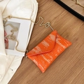Orange crocodile textured envelope crossbody bag with gold chain strap on a desk - Orange