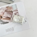 Close-up of white quilted AirPods pouch with button closure and circular ring hook - Small Bow Beige