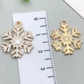 Golden snowflake charm with white enamel detail shown against a metric ruler for 2.5cm scale - White Snowflake 18x22mm