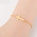 Close-up of a minimalist golden cross bracelet on a female wrist with delicate chain link - Cross / Gold