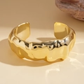 Dettaglio macro del bracciale rigido dorato largo con trama lava e finitura metallica ondulata - Oro