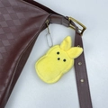 Detail eines gelben Plüsch-Hasenanhängers an einer braunen karierten Ledertasche - Gelb