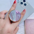 Pink pearl shell phone grip with gold rim attached to a smartphone being held by a hand - Gold Round Collapsible Socket Grip / Purple Scallop Shell