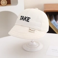 Close-up of beige cotton kids baseball cap featuring black TAKE embroidery and KUKUJI label - 50cm 1-3 Years / White