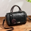 Vintage black cylinder pillow bag with brown straps and rose charm on wood table - Black