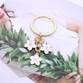 Detailed macro of gold keychain featuring three pink and white enamel cherry blossoms - White