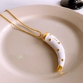 Detail shot of a bohemian gold necklace with a white horn pendant in a ceramic tray - Gold & White Polka Dot Style