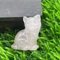 Close-up of a cute 1.2-inch natural pink crystal cat figurine on green grass and wood - Rose Quartz
