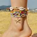 Detail van een bohemien enkelbandje met schelpkralen en gouden zeesterren op strand - Enkelbandje Set / Multicolor Enkelband Set