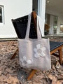 Detail of a beige knitted tote bag with white flower appliques hanging on a wooden chair - Khaki