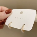 Elegantes pendientes de aro dorados con una hilera de pequeñas perlas blancas, en la mano - Pendientes de aro de perlas / Dorado