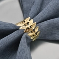 Golden leaf metal napkin ring featuring an intricate leaf design on a blue linen napkin - Leaf / Gold