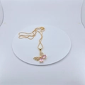 Vergulde vlinderketting met roze edelstenen gepresenteerd op een witte display - Ketting met Hanger / Roze Vlinder