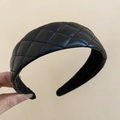 Detail of black quilted leather headband with thick padding held against beige background - Quilted Wide Style (Headband-Black) / Black